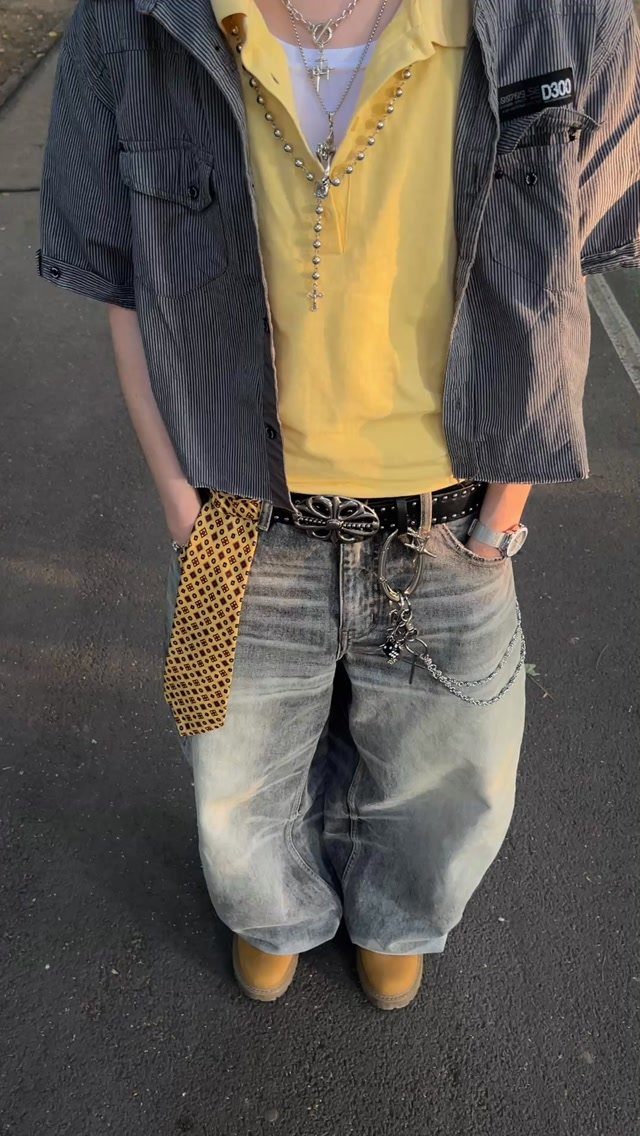 A person wearing baggy jeans, a yellow shirt, and multiple silver necklaces and chains.