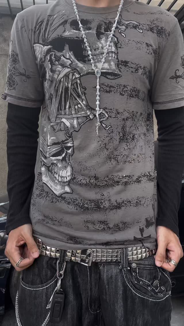 A person wearing a grey graphic t-shirt with skull prints and a studded belt.