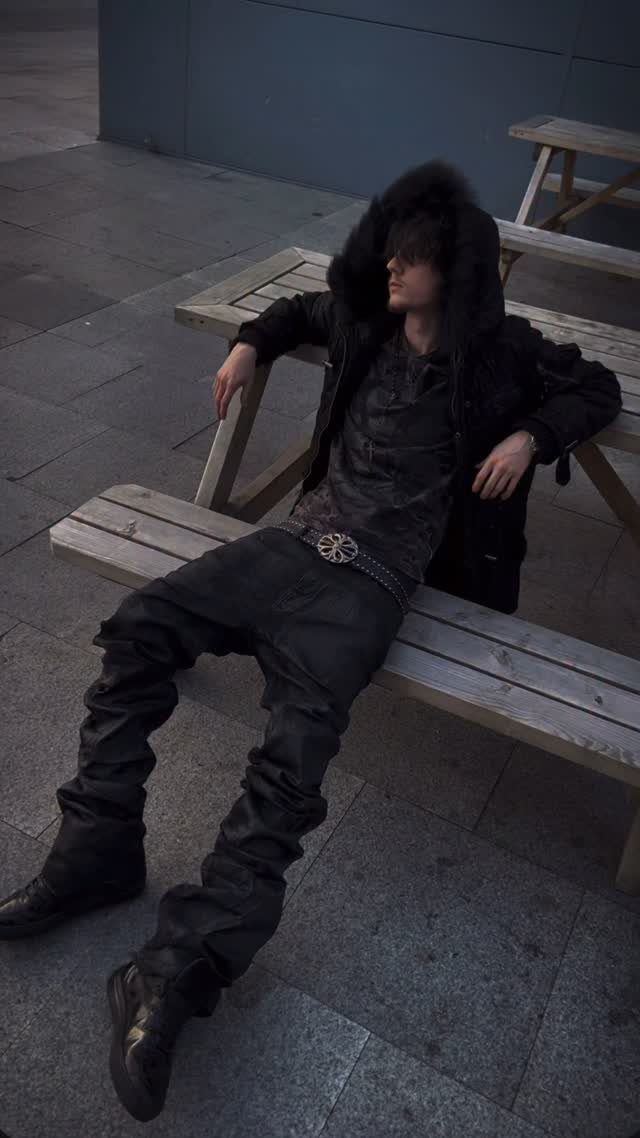 A person wearing an all-black outfit sitting on a wooden picnic bench outdoors.