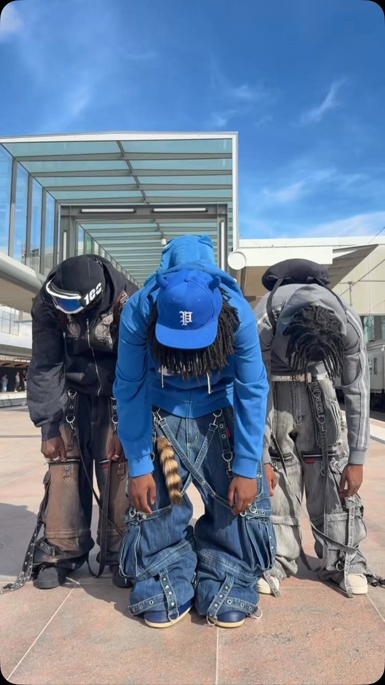 Three people leaning forward to display their baggy, multi-pocket denim cargo pants with chains.