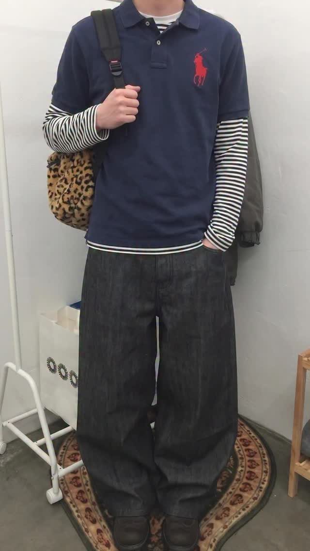 A person wearing a navy polo over stripes with baggy dark denim jeans.