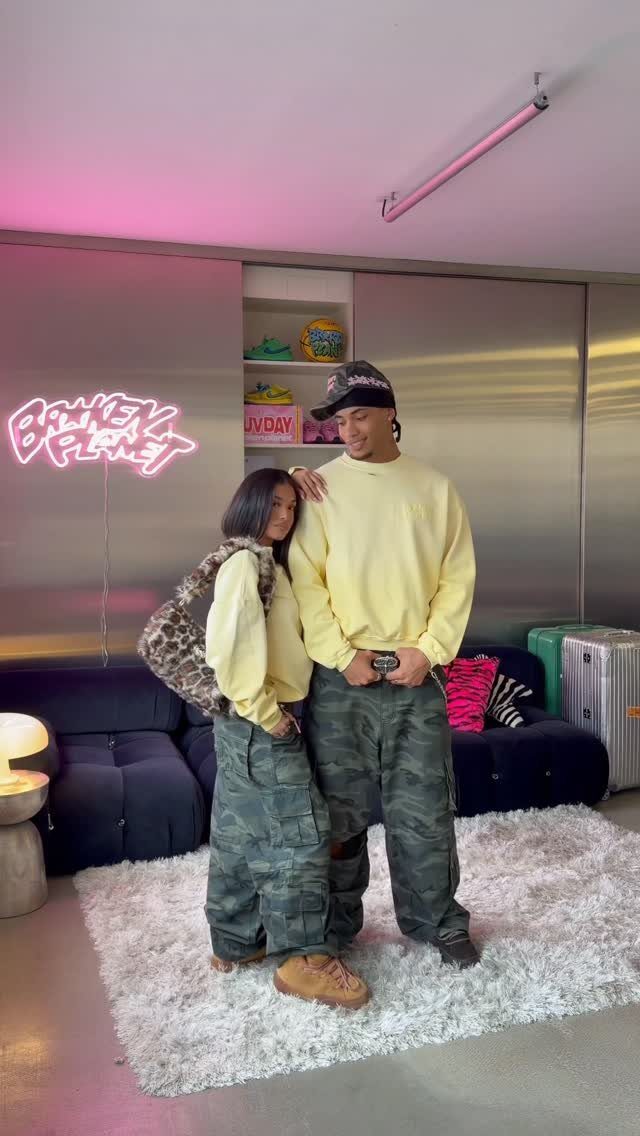 A man and woman posing in baggy yellow sweatshirts and camouflage pants.