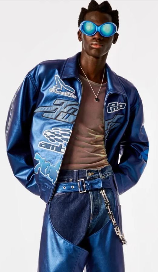 A person wearing blue futuristic sunglasses, a metallic blue bomber jacket, and matching blue pants.