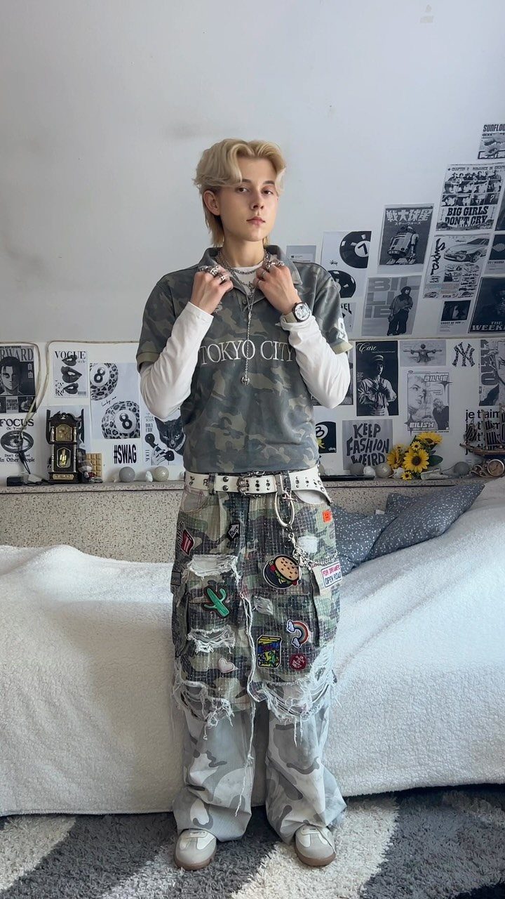 A young man posing in camouflage cargo pants with patches and white belts.