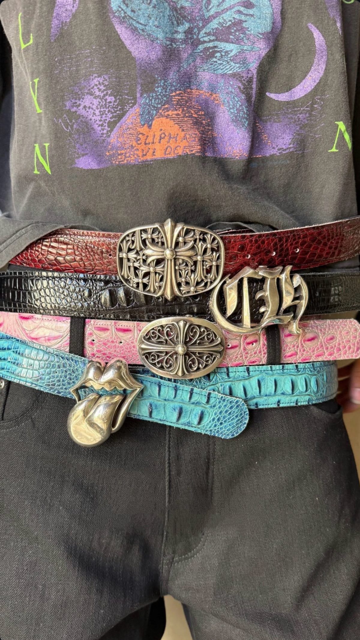 Several textured, colorful belts with large silver buckles layered over a person's waist.